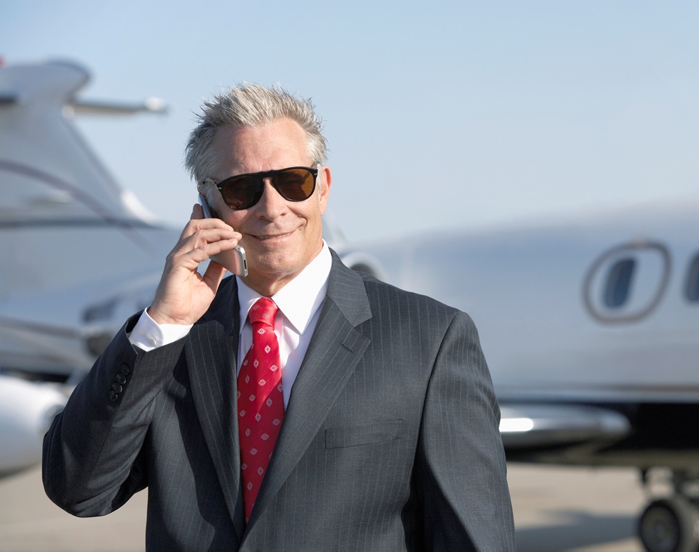 Businessman on phone standing in front of private jet at private airport