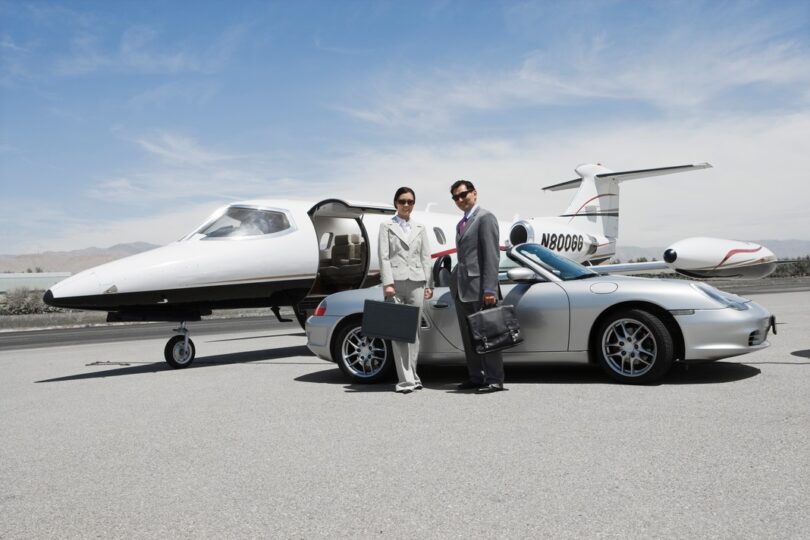 Two people in front of a car and private jet.